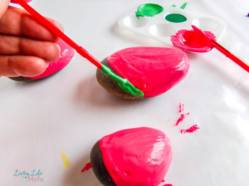 painting the green onto the bottom of the watermelon painted rock with a paintbrush.