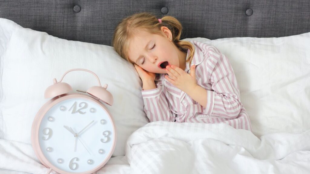 young child waking up with an alarm clock on the bed